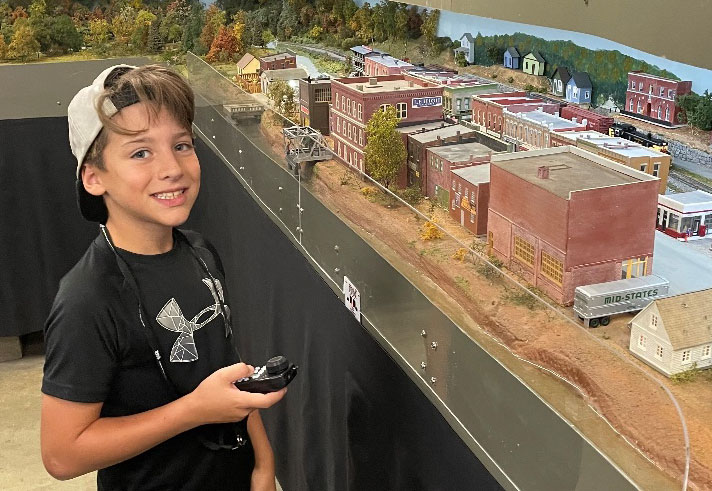 photo of young boy smiling next to a model railroad